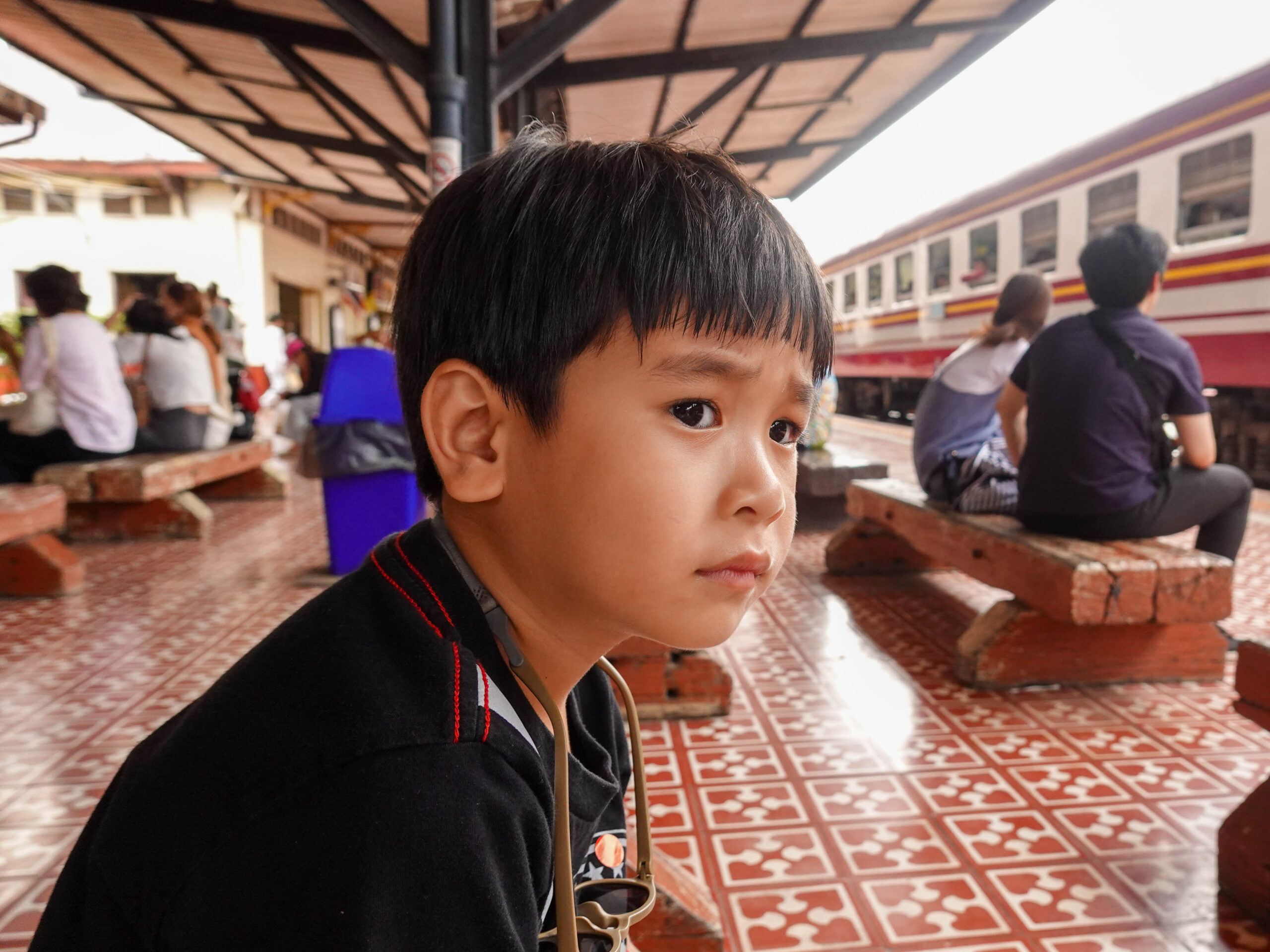 เด็กนั่งที่สถานีรถไฟ มีรถไฟกำลังวิ่งผ่าน