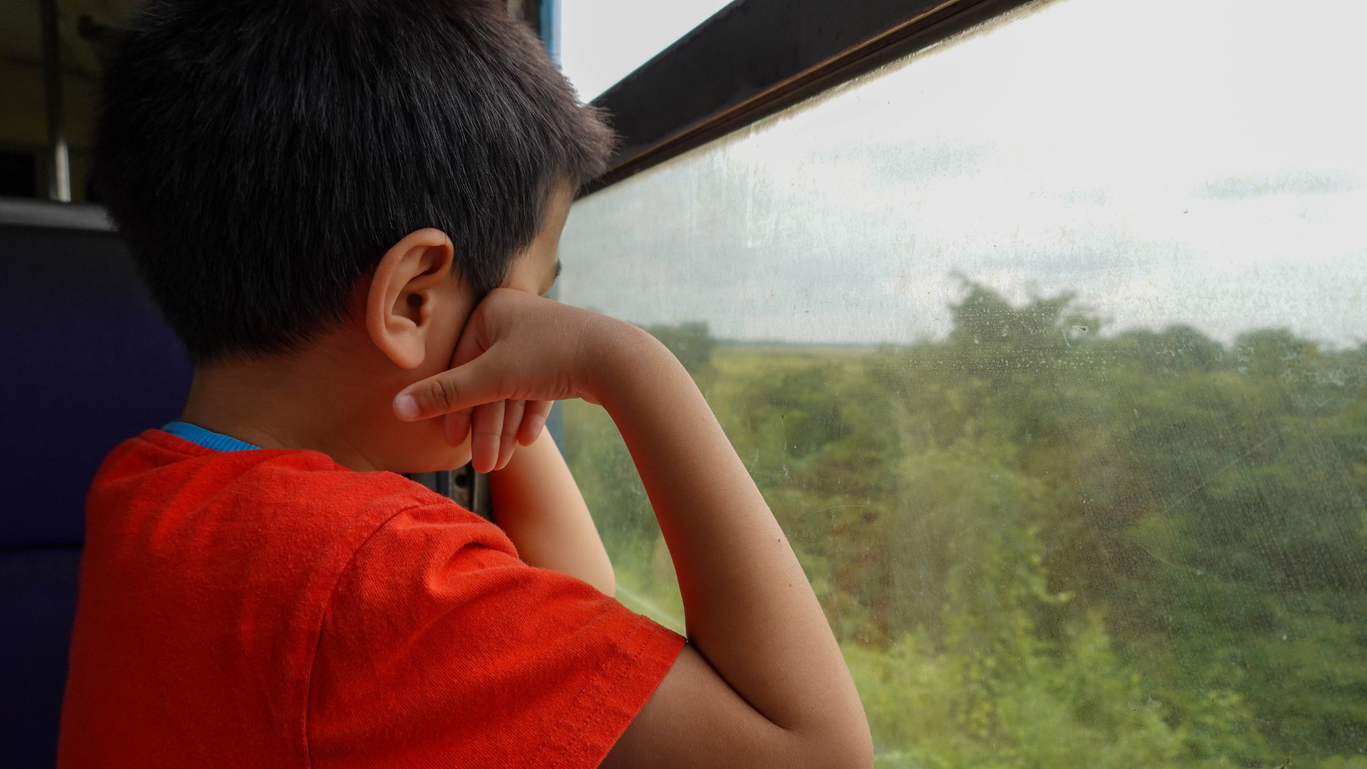 kid on a train looking outside from window of a train